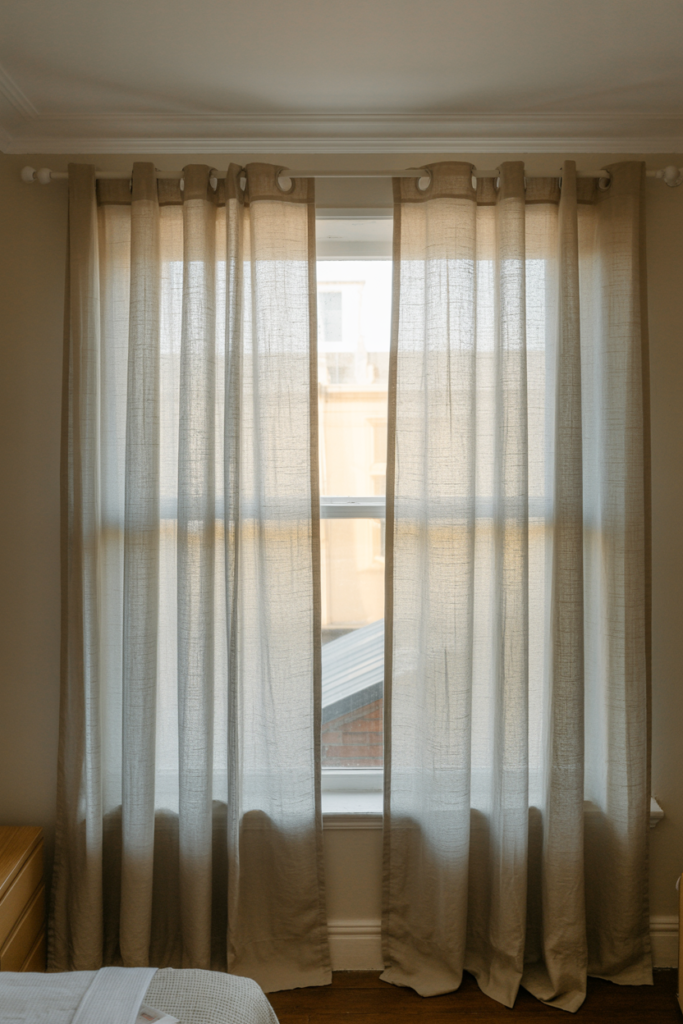 Sheer white floor-length curtains hung at ceiling height in a small bedroom to create the illusion of taller walls and more space