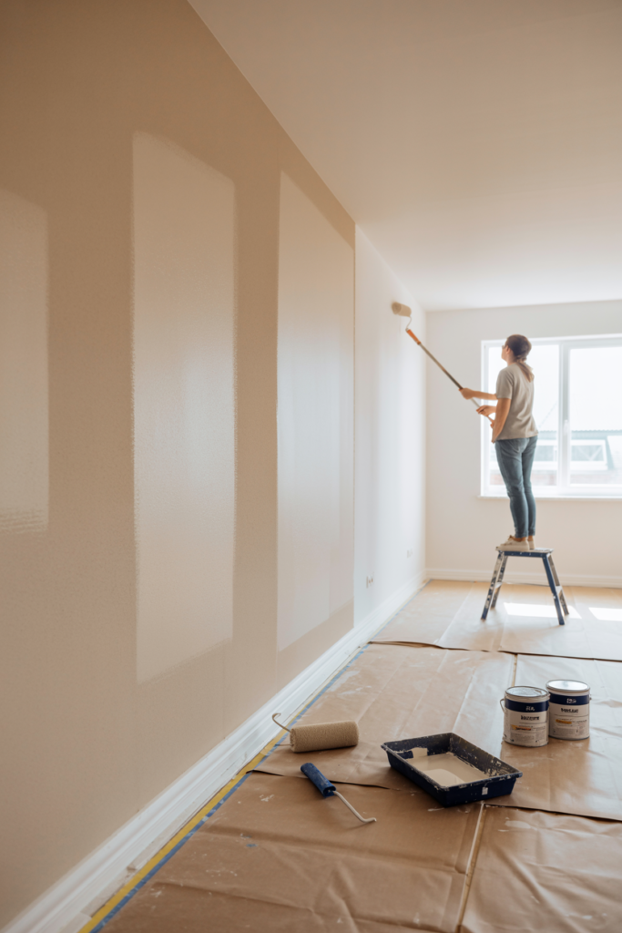 Person painting freshly plastered walls in warm white during budget garage conversion decorating stage