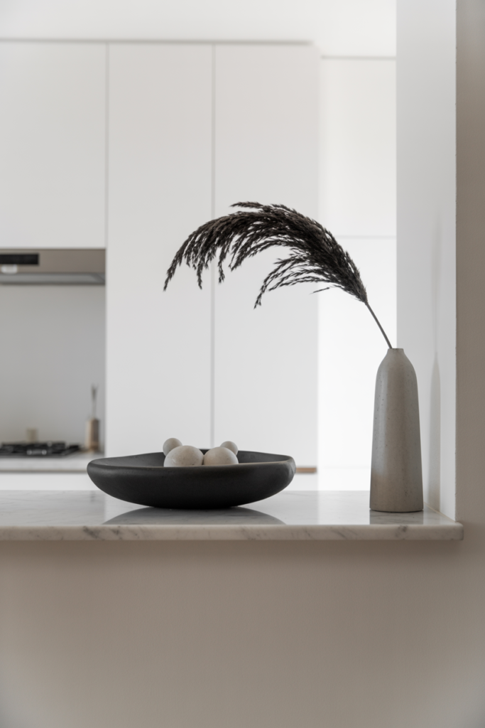 Minimal modern half wall ledge with matte ceramic decorative bowl and tall concrete vase holding a single dried pampas stem